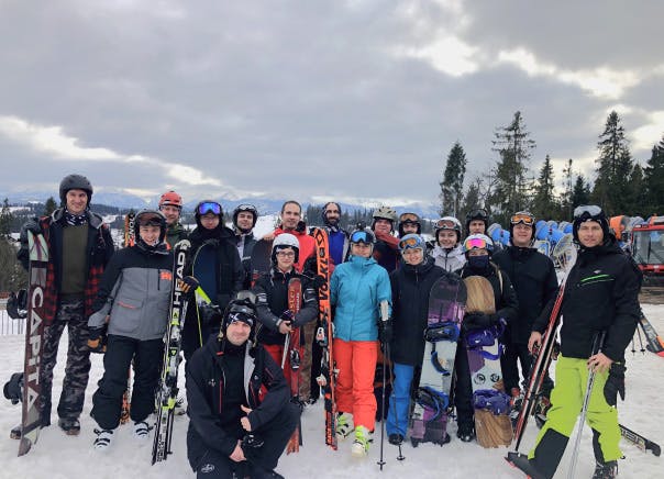 A group photo of the Xfive team on the slope in Slovakian Tatras. Some members of the team have skis, and some of them have snowboards.